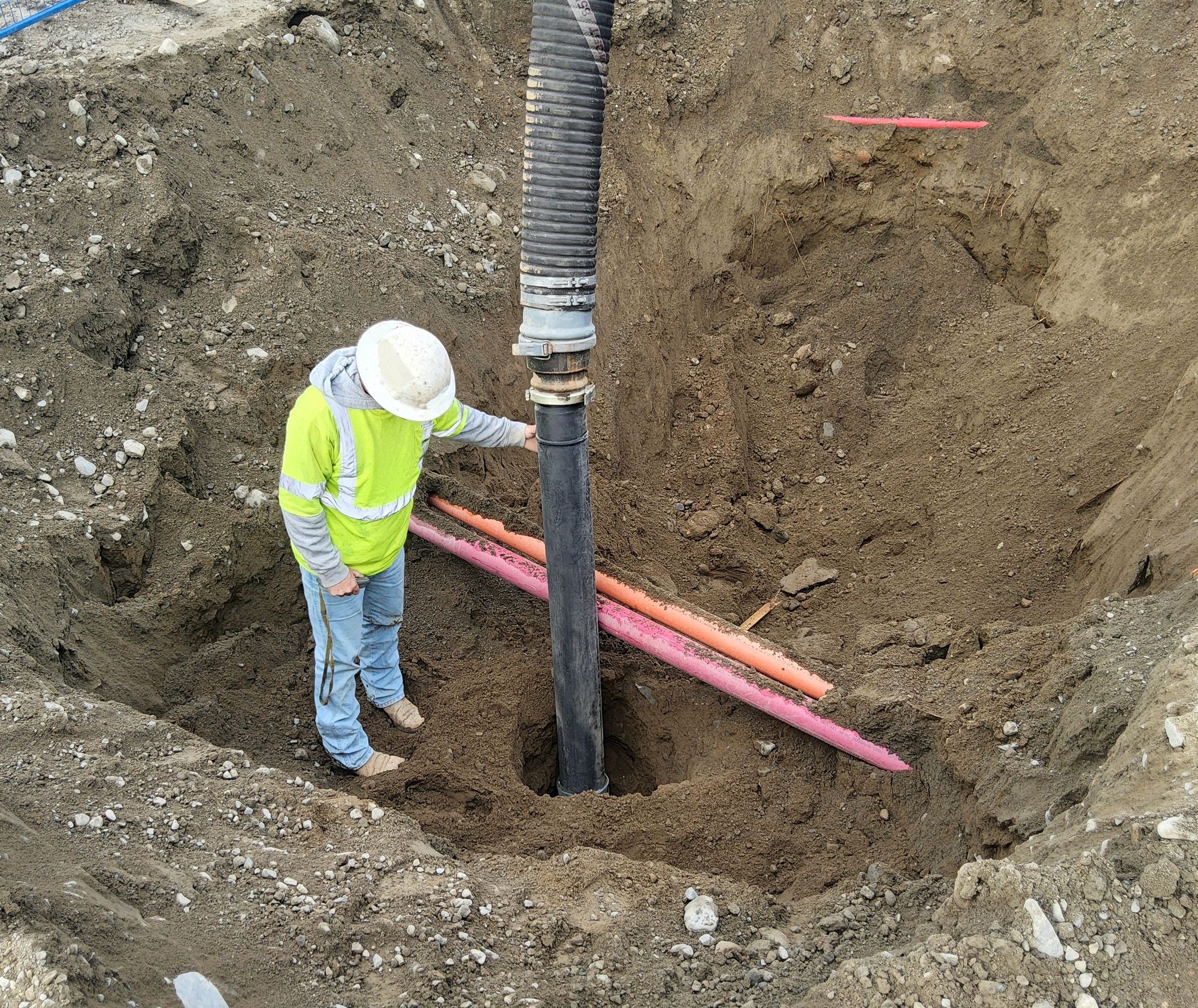 Civil worker inspects hydrovac excavation exposing underground utility ducts to safely daylight utilities before trenching.